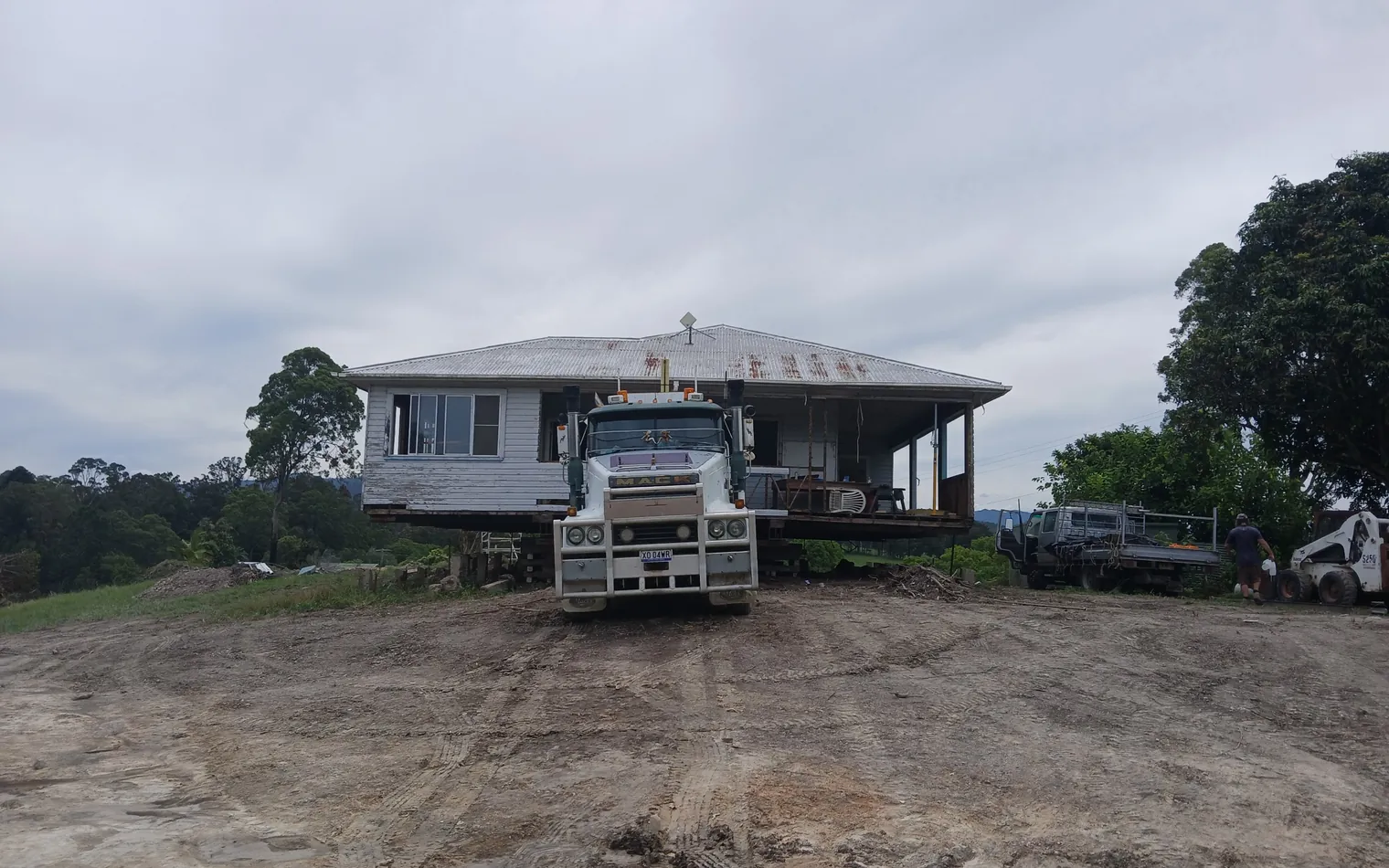 Truck hauling a cream weatherboard home on a hydraulic trailer beside a river